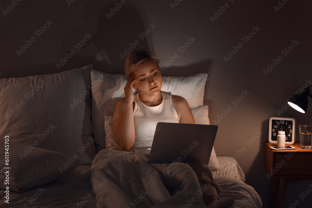 Sleepy young woman using laptop in bed at night