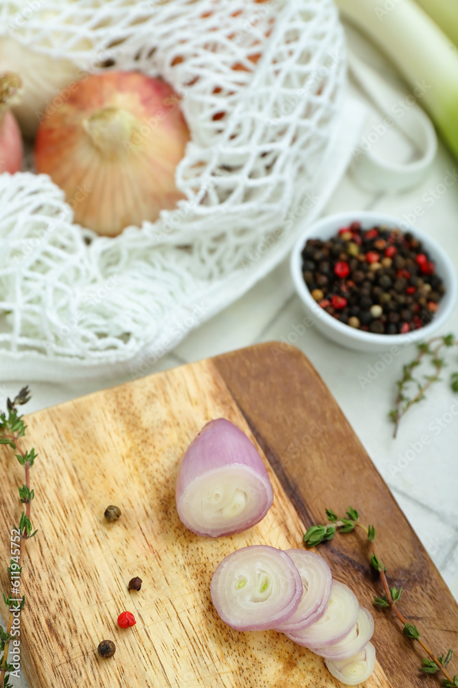 Wooden board and string bag with different kinds of onion on white tile background