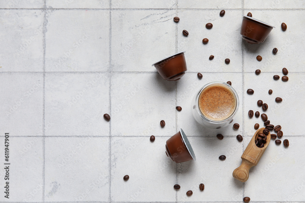 Cup of delicious espresso, pods and beans on white tiled table