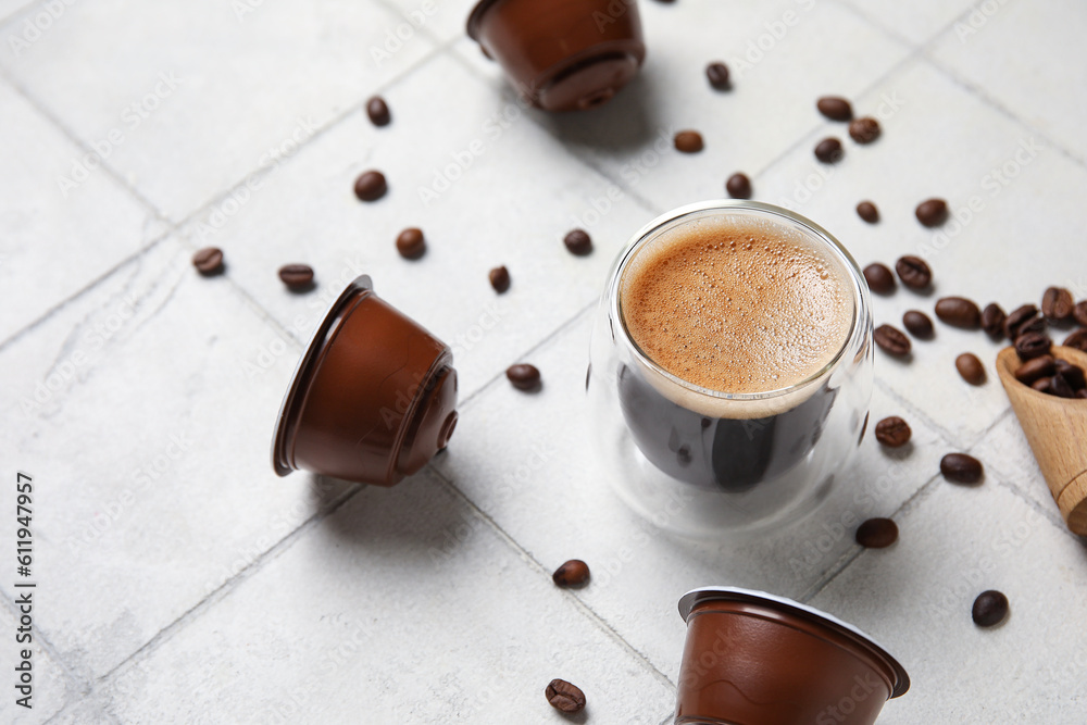 Cup of delicious espresso, pods and beans on white tiled table