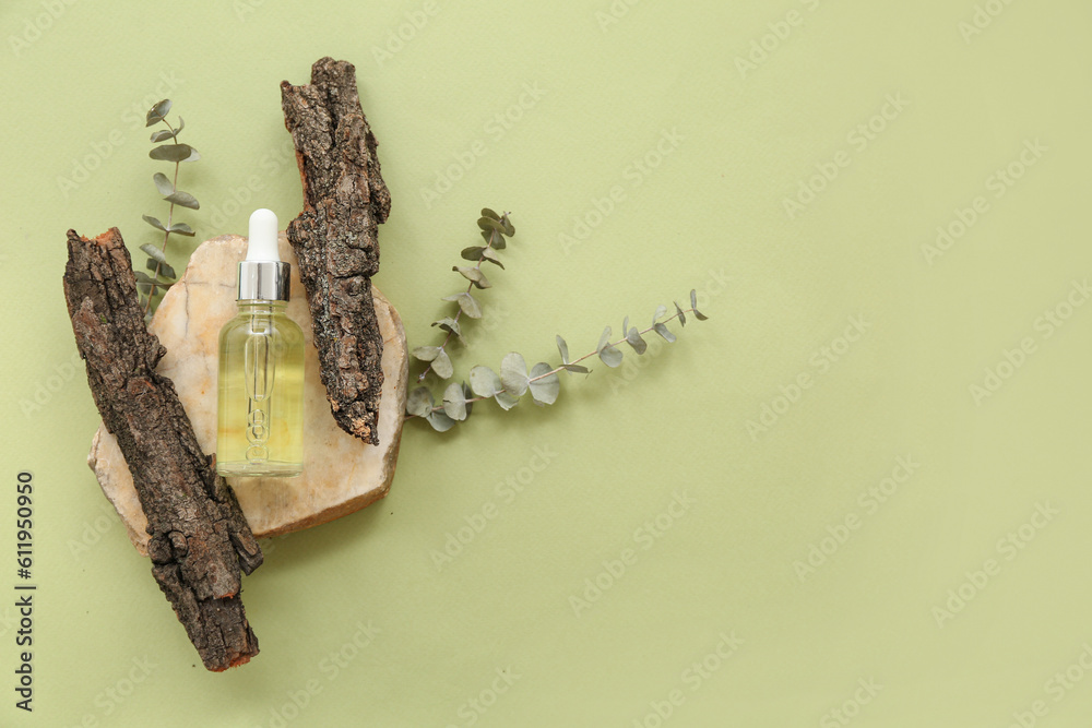 Composition with bottle of essential oil, tree bark, stone and eucalyptus branches on color backgrou