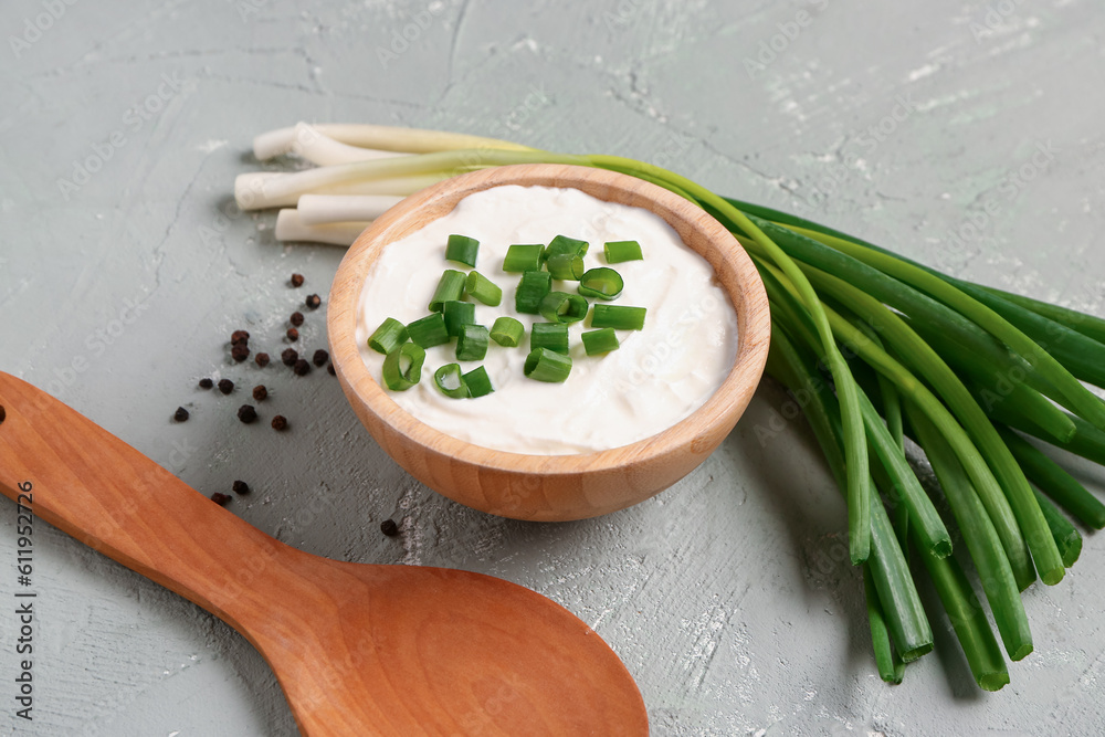 Bowl of tasty sour cream with sliced green onion and peppercorn on grey background