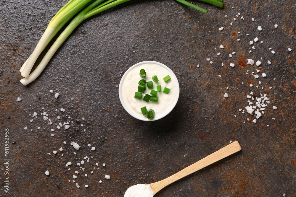 Bowl and spoon of tasty sour cream with sliced green onion on dark background