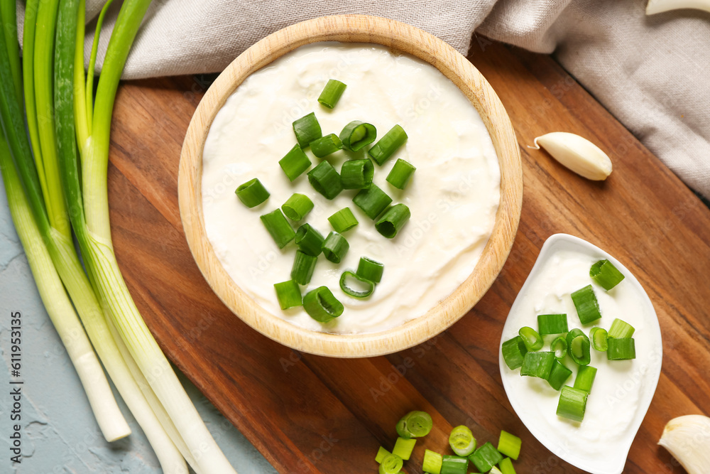 Bowl and gravy boat of tasty sour cream with sliced green onion on blue background