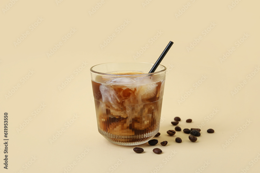 Glass of ice coffee with straw and beans on yellow background