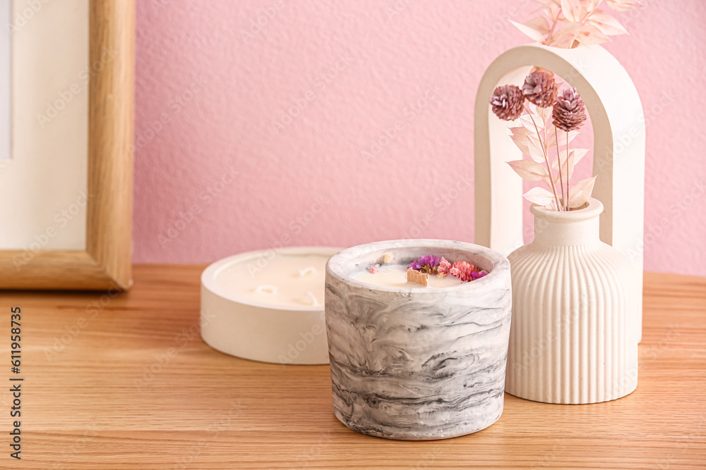 Holders with candles and decor on table near pink wall in room, closeup