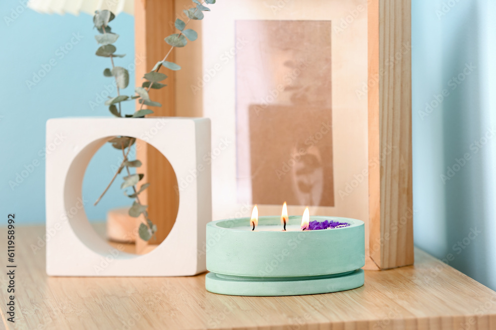 Holder with burning candle and decor on table near blue wall in room, closeup