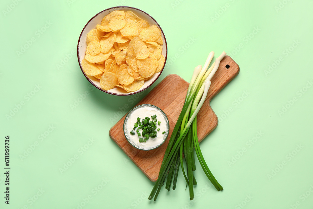 Bowl of tasty sour cream with sliced scallion and potato chips on green background