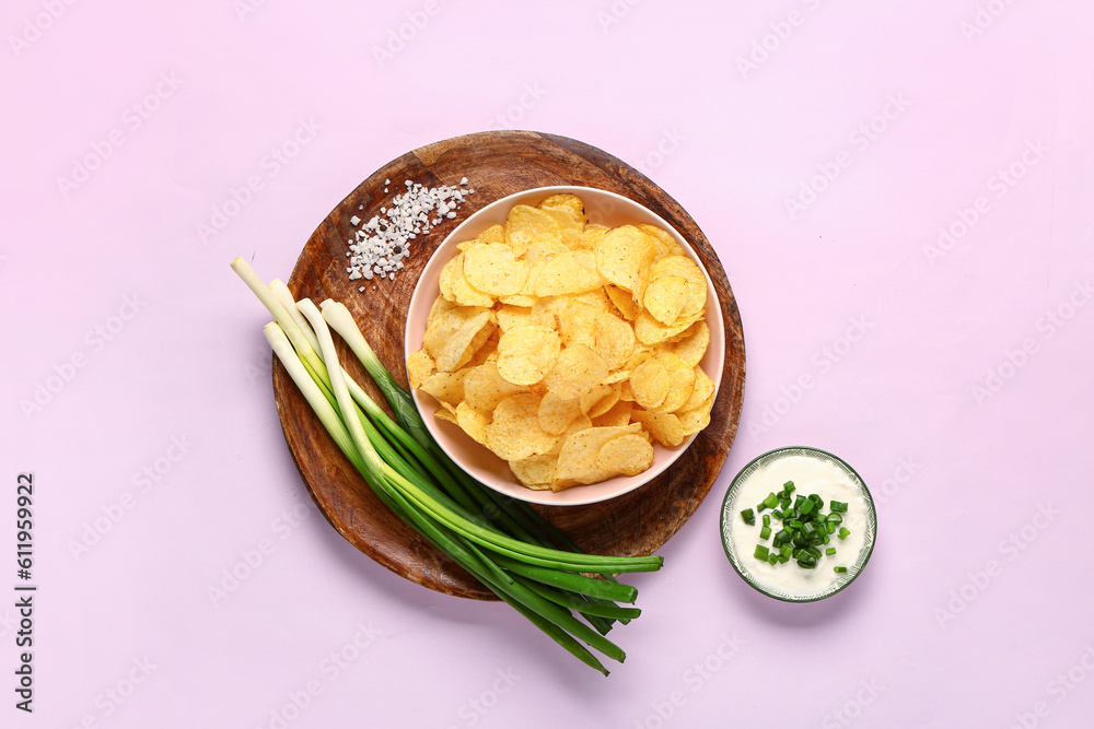 Bowl of tasty sour cream with sliced green onion and potato chips on lilac background