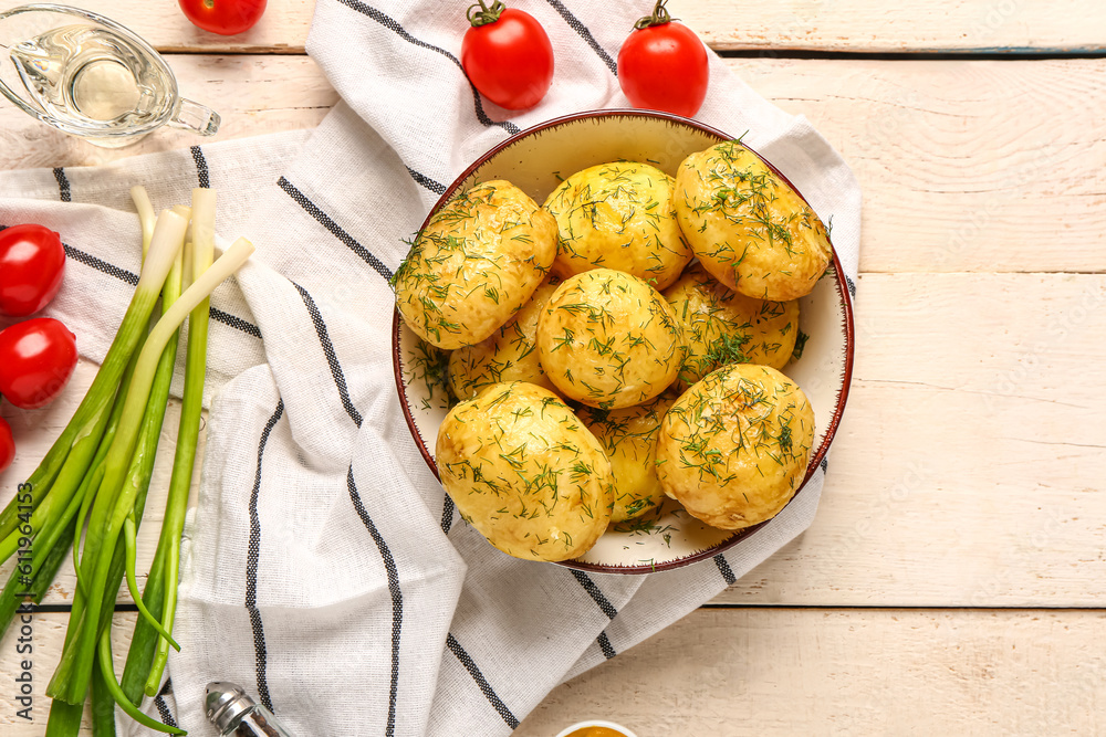 Plate of boiled baby potatoes with dill and tomatoes on white wooden background