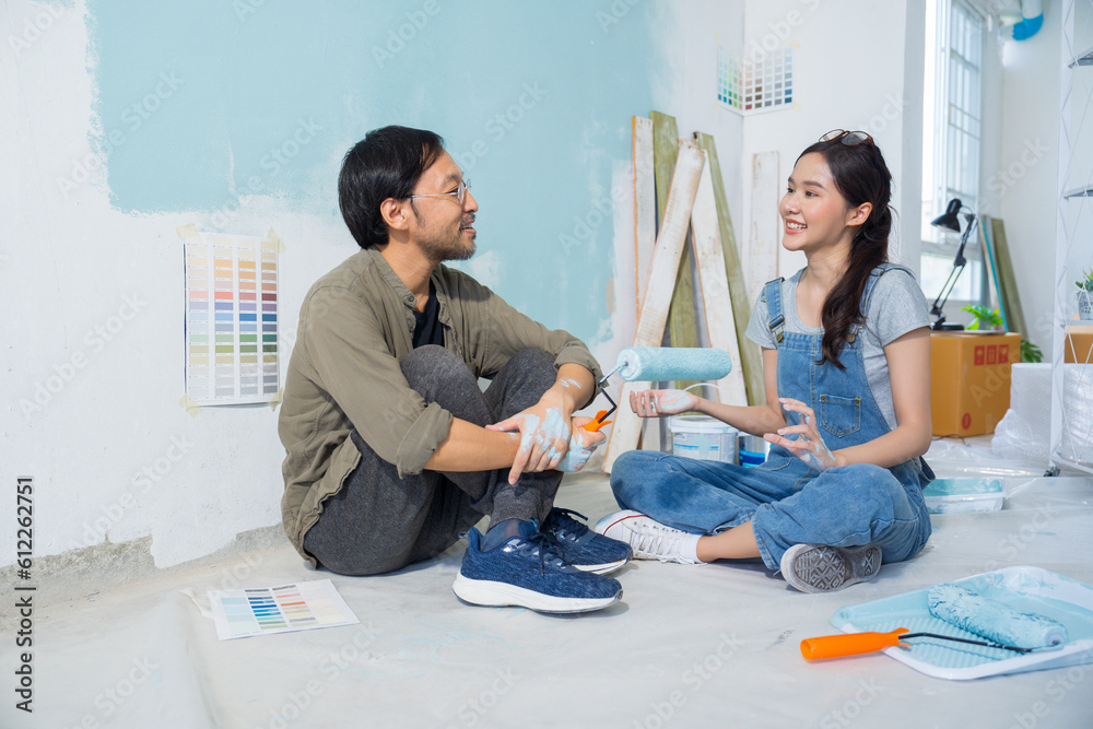 Asian couple talking chatting while taking a break from painting the walls of their house.