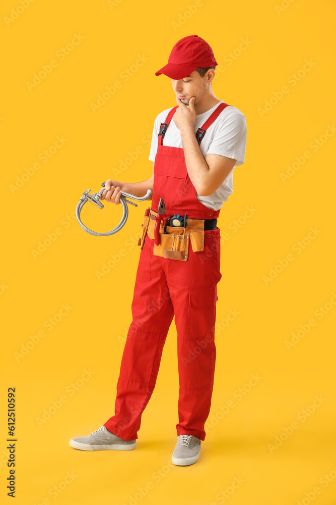 Thoughtful young plumber with flexible hose on yellow background