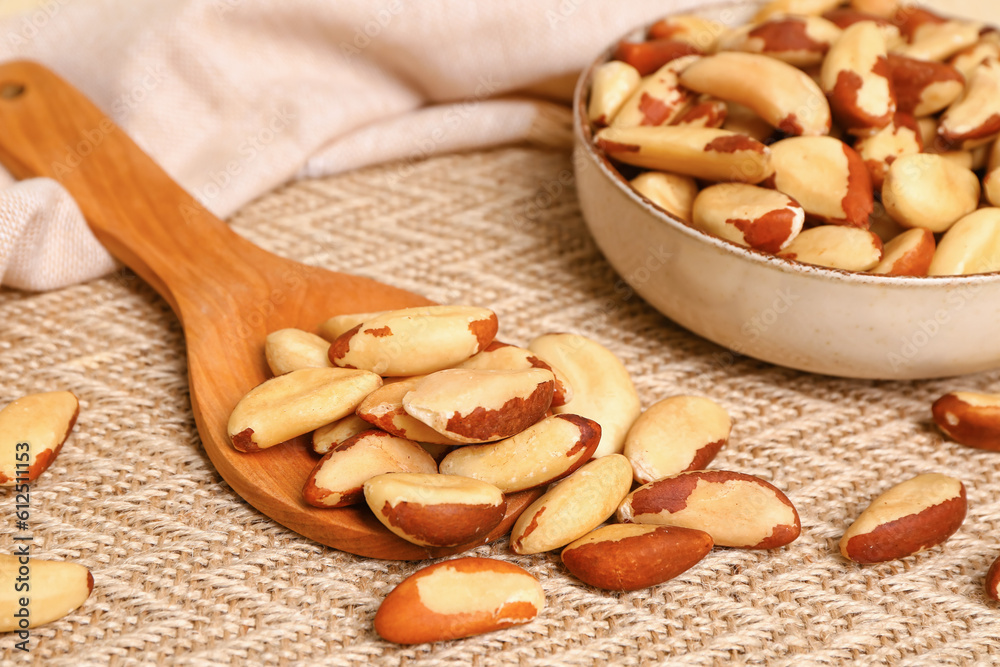 Spoon and bowl of tasty Brazil nuts on fabric background, closeup