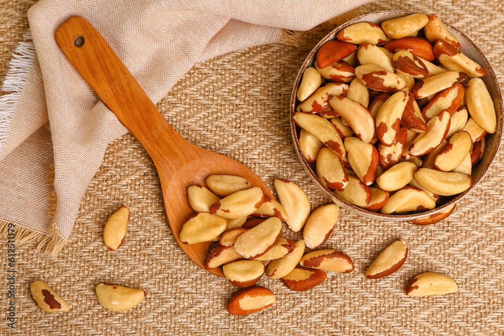 Spoon and bowl of tasty Brazil nuts on fabric background