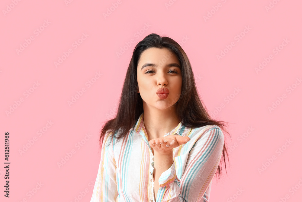 Young woman in shirt blowing kiss on pink background