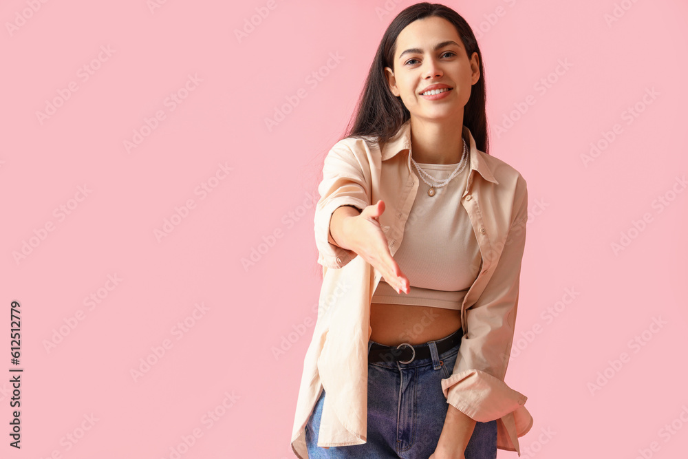 Young woman in shirt reaching out for handshake on pink background