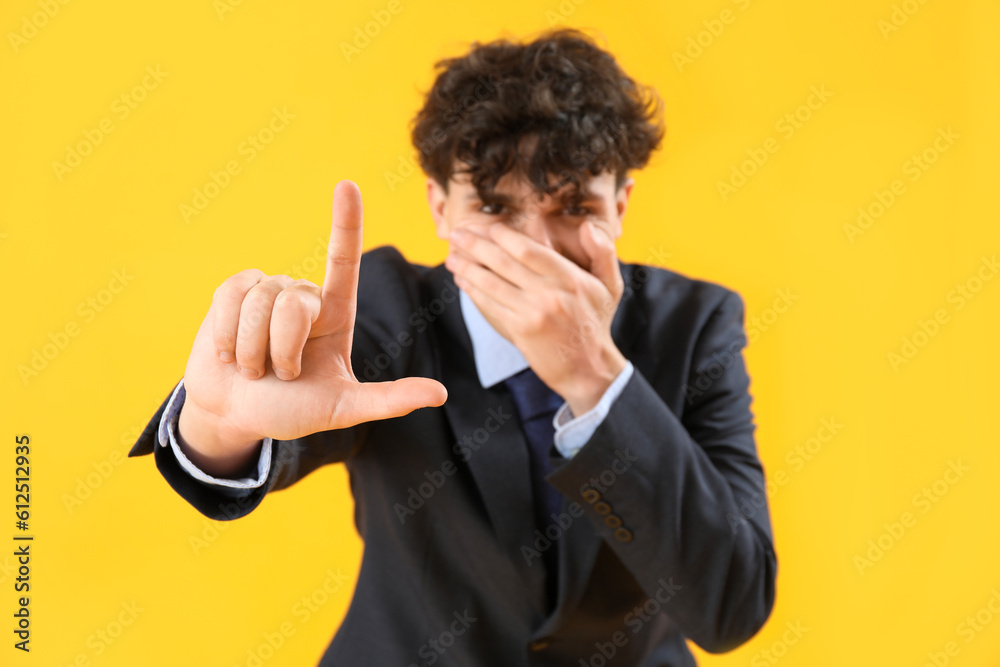 Laughing businessman showing loser gesture on yellow background