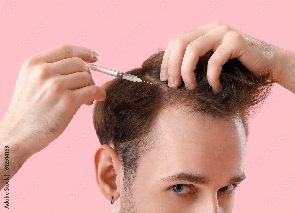 Young man making injection for hair growth on pink background, closeup