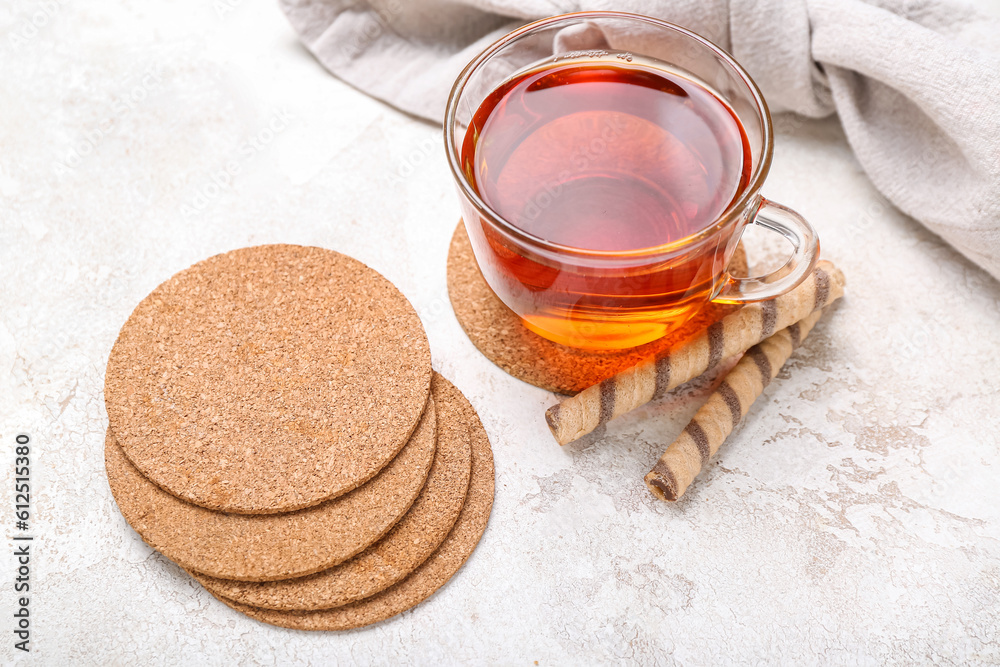 Drink coasters with cup of tea and wafer rolls on white table