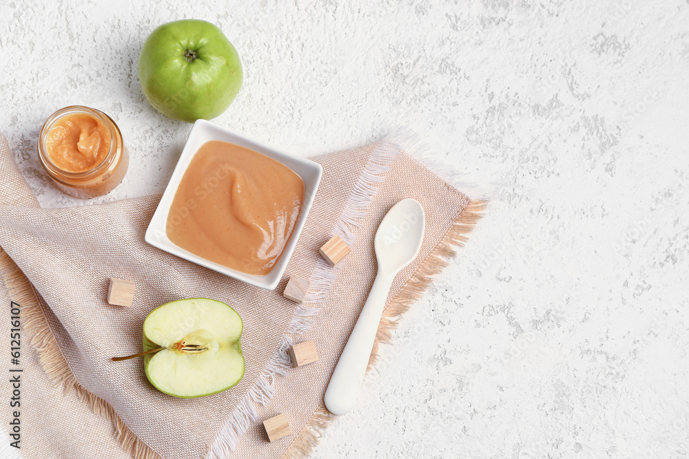 Bowl of healthy baby puree, fresh apples and wooden cubes on light background