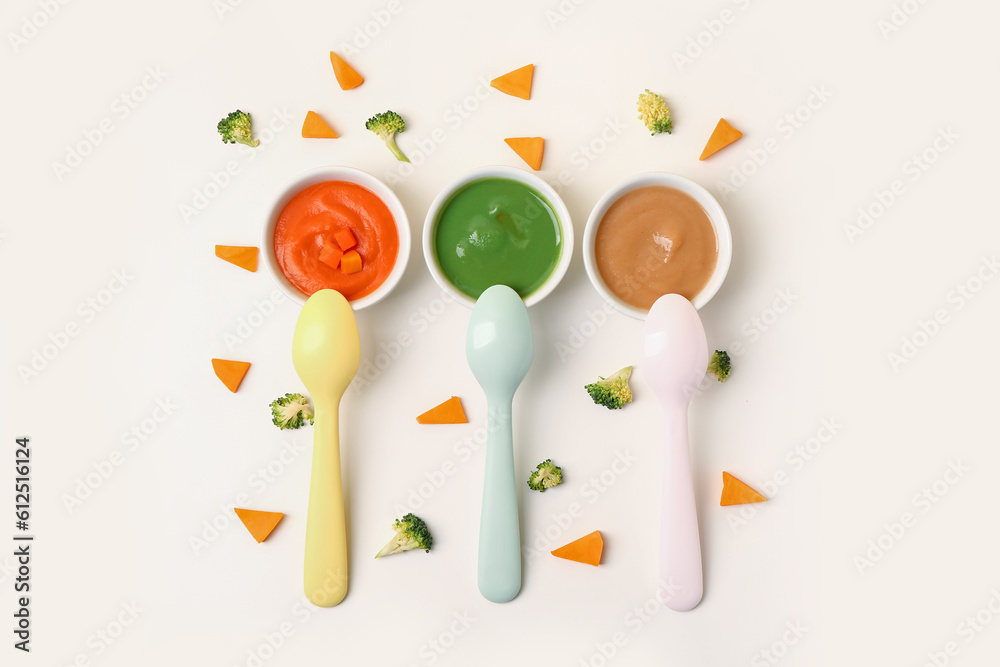 Composition with bowls of healthy baby puree and cut vegetables on white background