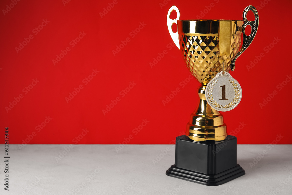 Gold cup with first place medal on table near red wall