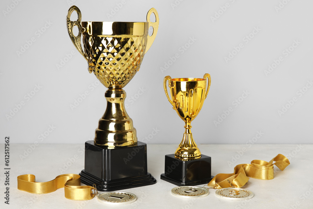 Gold cups with prize medals on table near grey wall