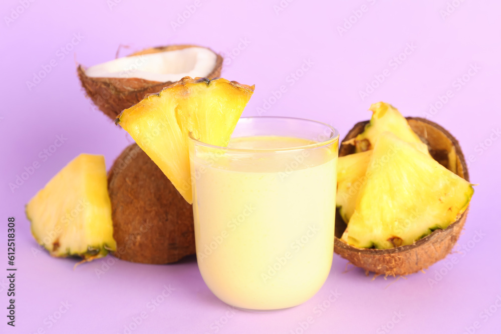 Glass of tasty pineapple smoothie and coconut on lilac background