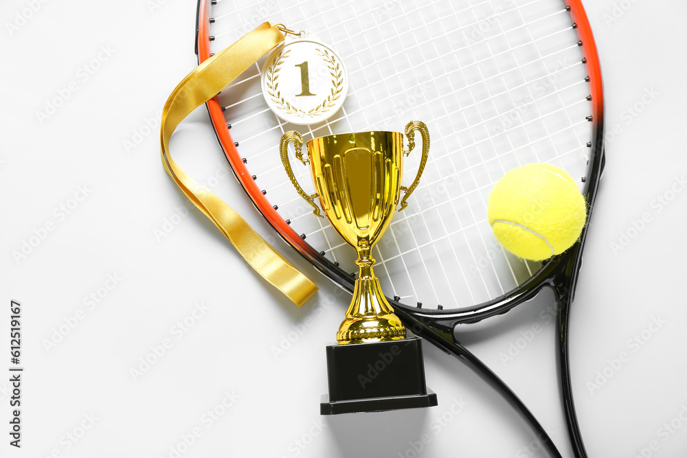 Gold cup with first place medal, tennis racket and ball on light background