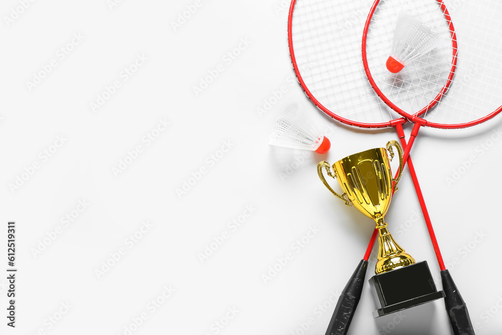 Gold cup with badminton rackets and shuttlecocks on light background