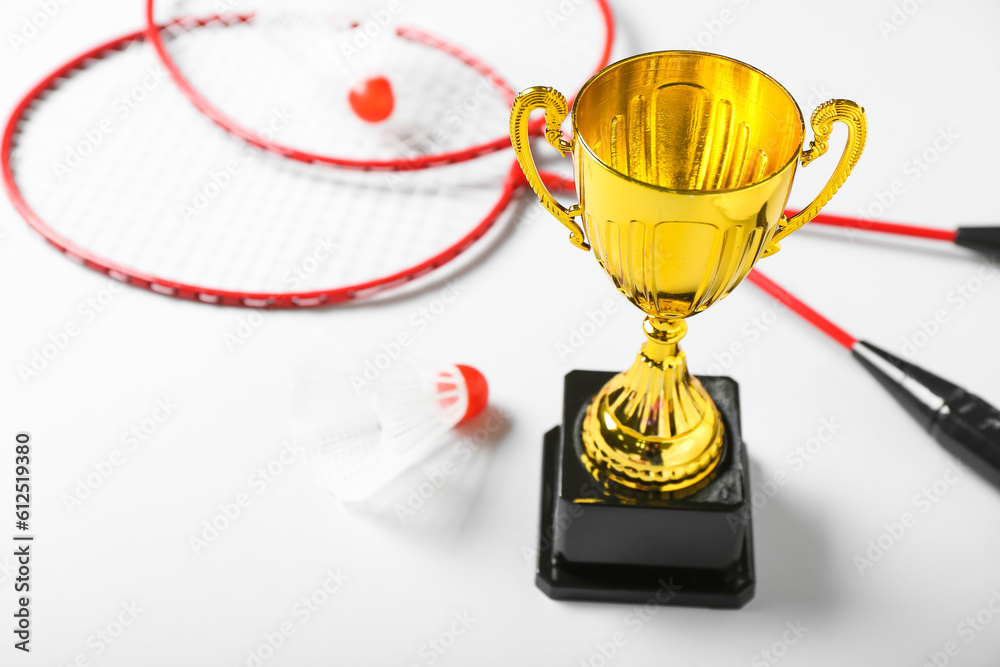 Gold cup with badminton rackets and shuttlecocks on light background, closeup