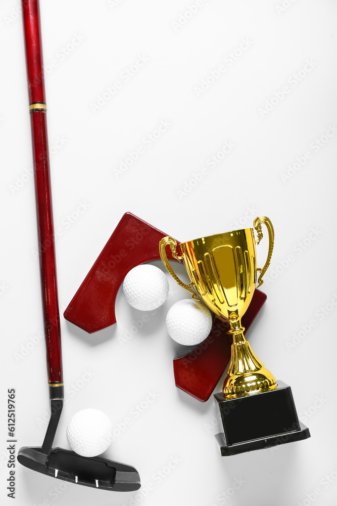 Gold cup with golf club and balls on light background