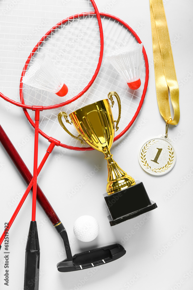 Gold cup with first place medal and sports equipment on light background