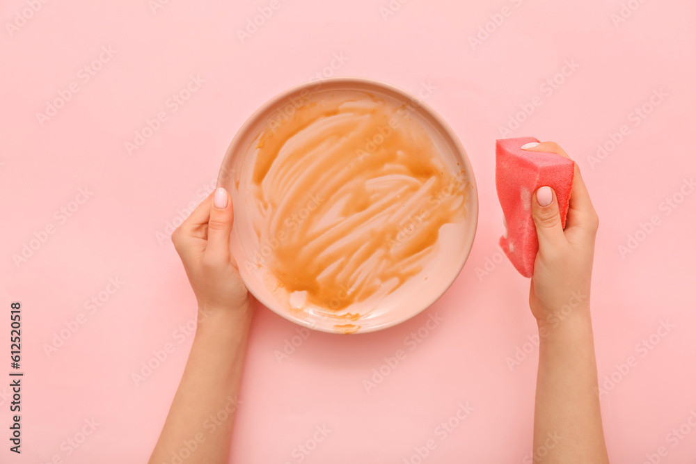 Female hands washing dirty plate with sponge on pink background