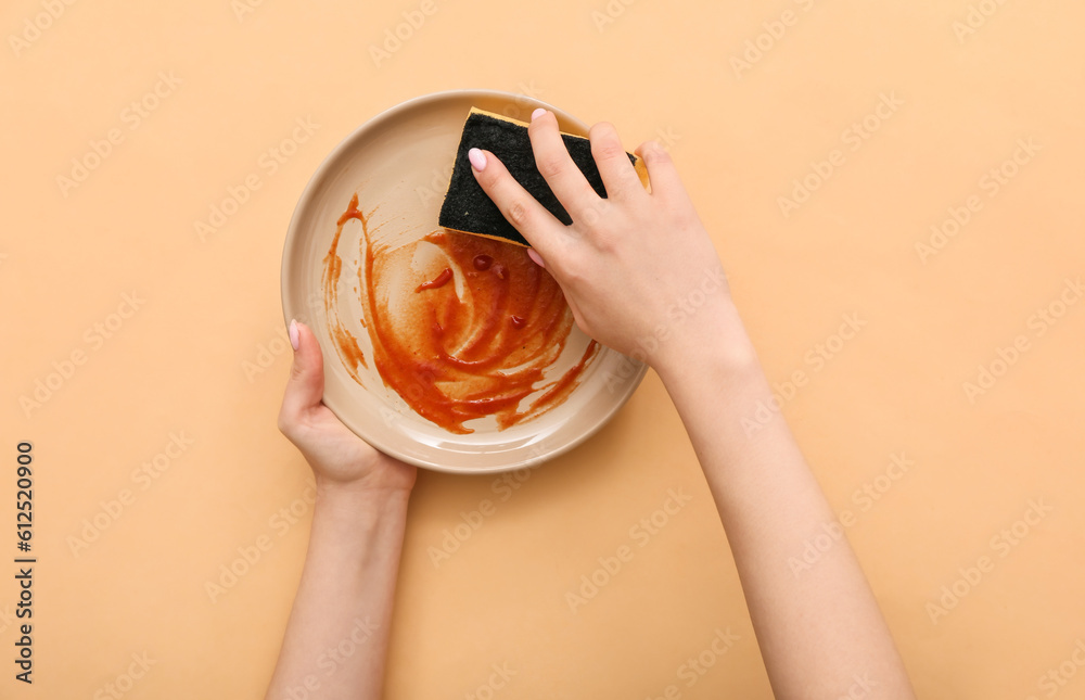 Female hands washing dirty plate with sponge on beige background