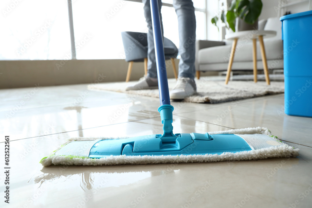 Male janitor mopping floor in living room, closeup