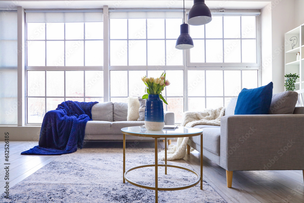 Interior of bright living room with cozy sofas and coffee table near big window