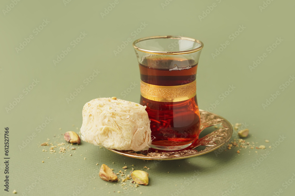 Plate with tasty Turkish Pismaniye and glass of tea on green background