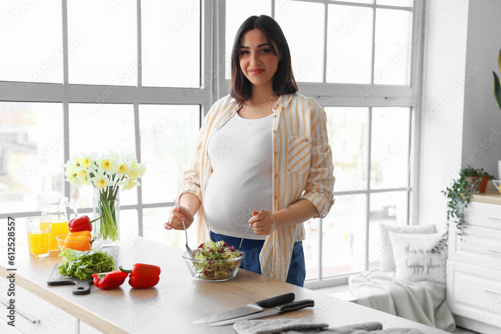 Young pregnant woman making vegetable salad in kitchen