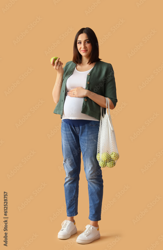 Young pregnant woman with apples on beige background