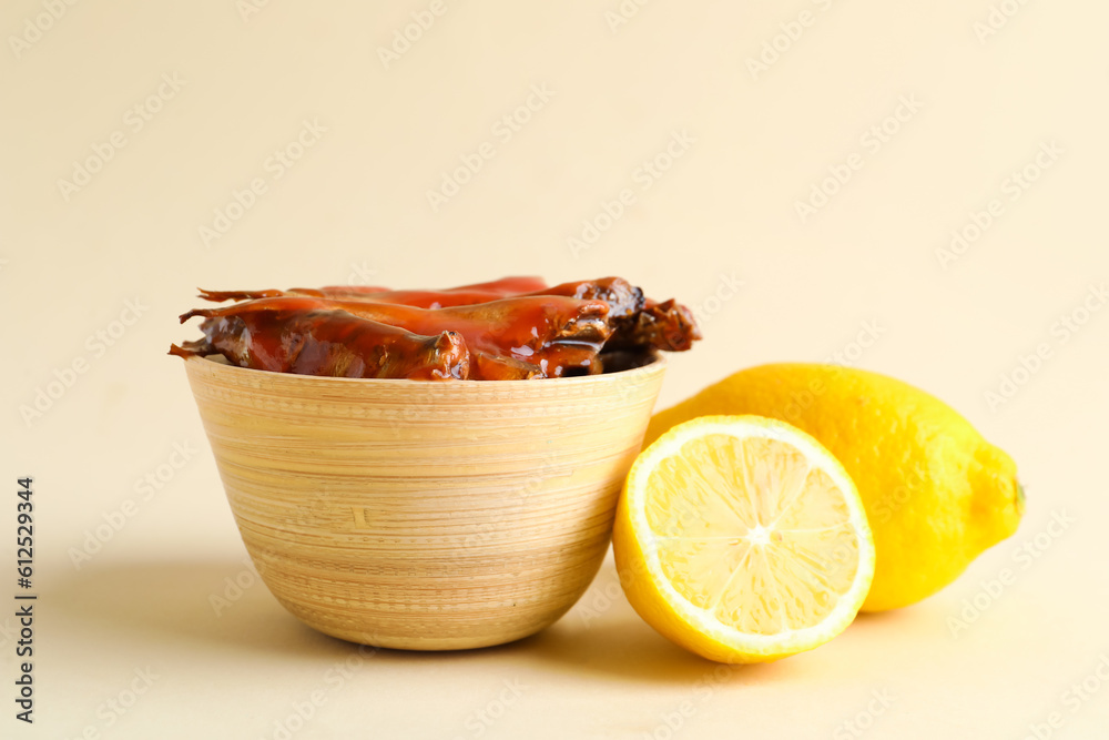 Bowl with canned fish in tomato sauce and lemons on beige background