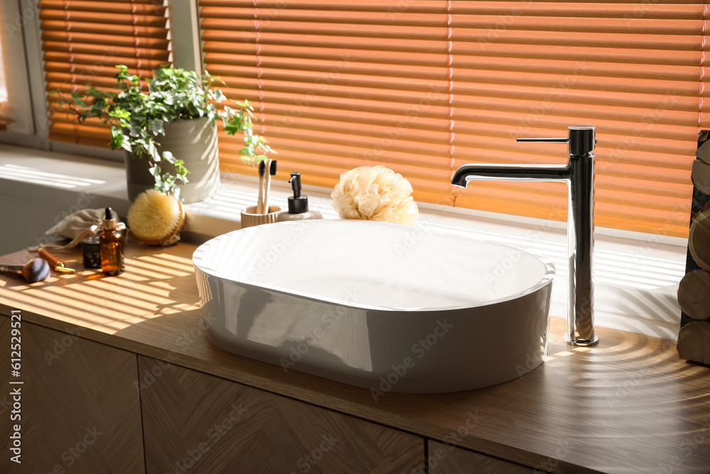 Sink with bath accessories on table near window in room