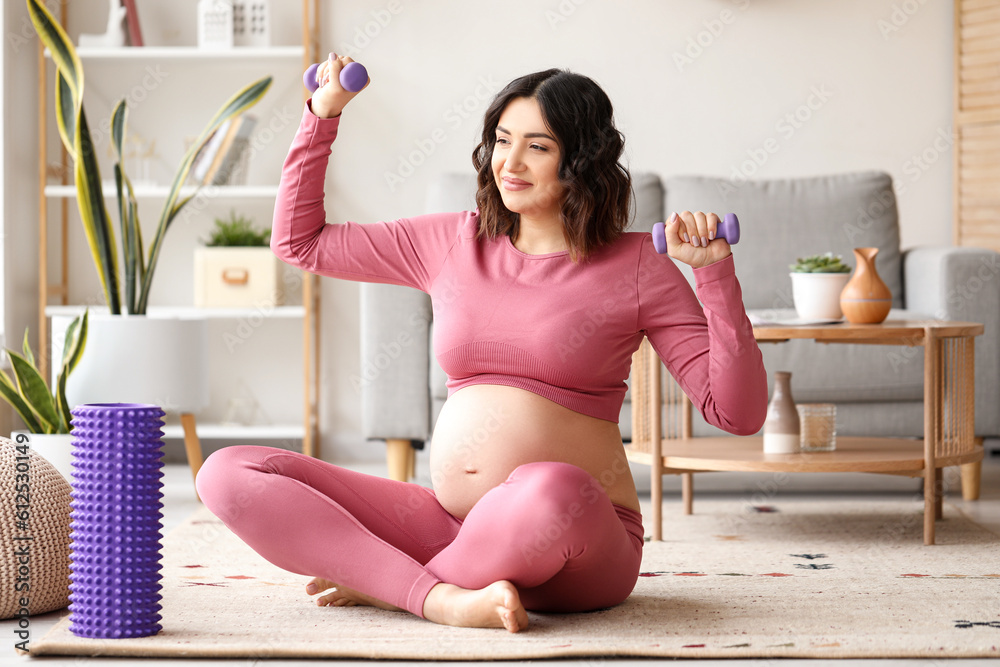 Sporty pregnant woman training with dumbbells at home