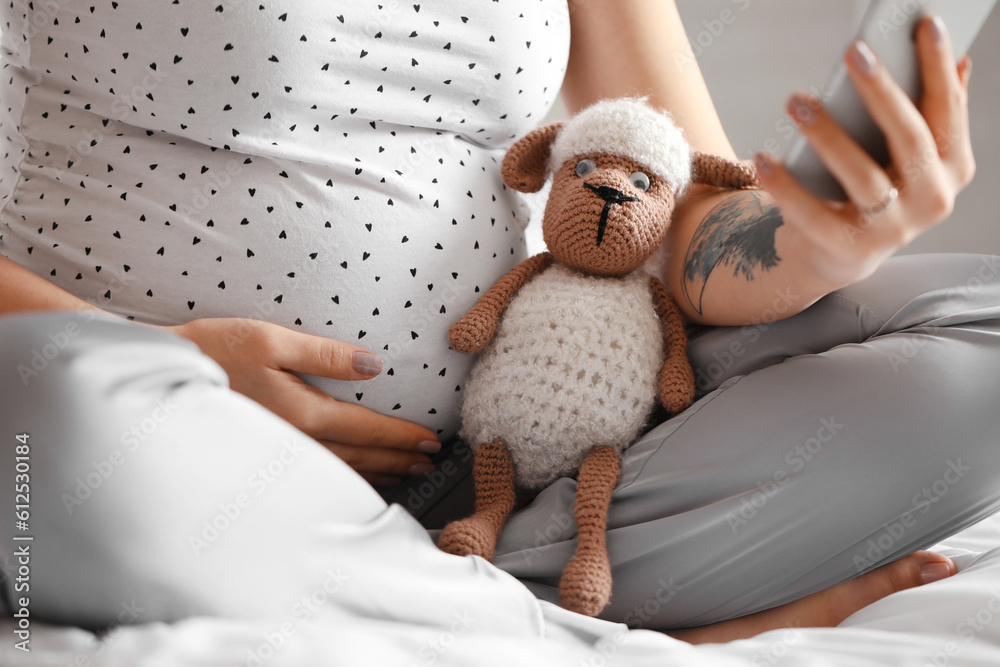 Young pregnant woman with toy using mobile phone in bedroom, closeup