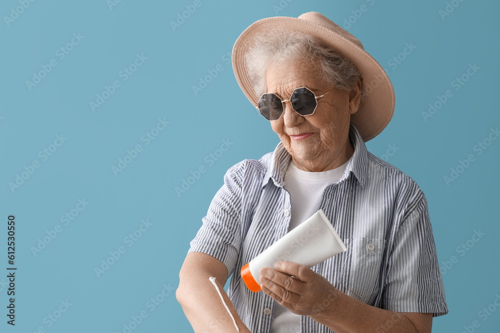 Senior woman applying sunscreen cream on blue background