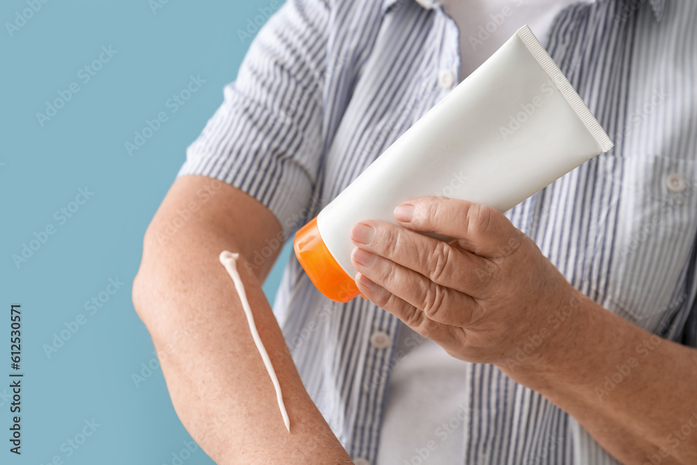 Senior woman applying sunscreen cream on blue background, closeup