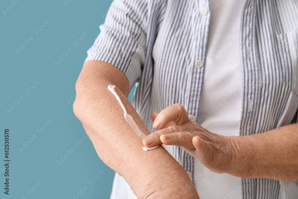 Senior woman applying sunscreen cream on blue background, closeup