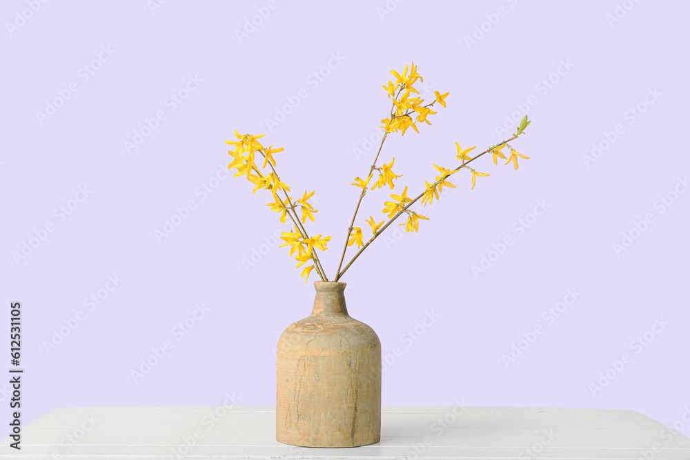 Vase with blooming tree branches on white table against lilac background