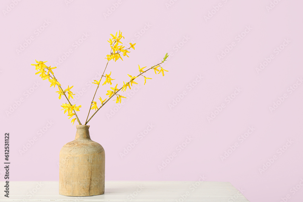 Vase with blooming tree branches on white table against pink background