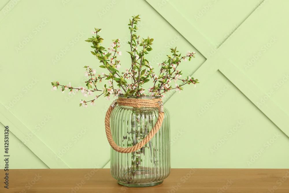 Vase with blooming tree branches on wooden table near green wall